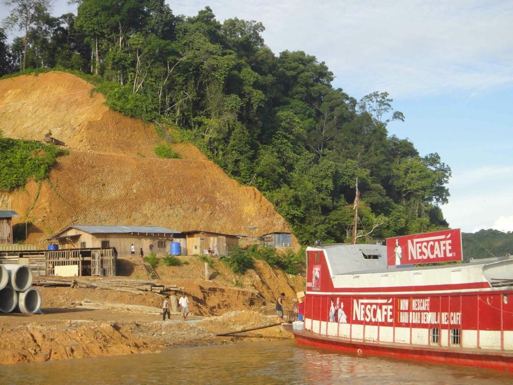logging_camp_batang_rejang_borneo Logging camp set against a scarred hillside on the banks of the Batang Rejang, with Nescafe branded delivery boat in the foreground.