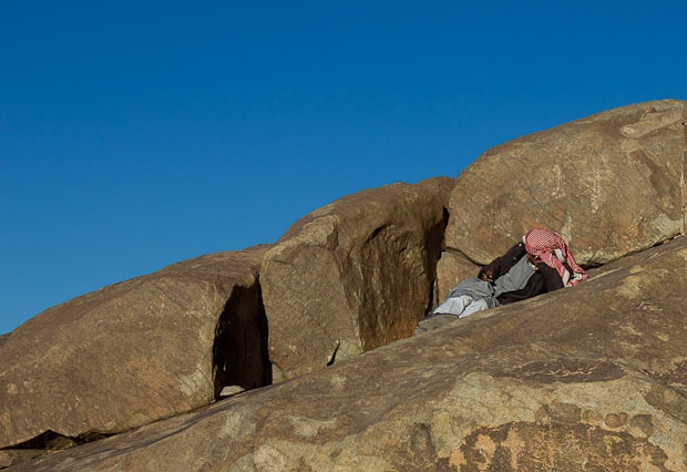Bedouin Man Texting on Mount Sinai Bedouin man in traditional dress reclines atop Mount Sinai, texting on his mobile.