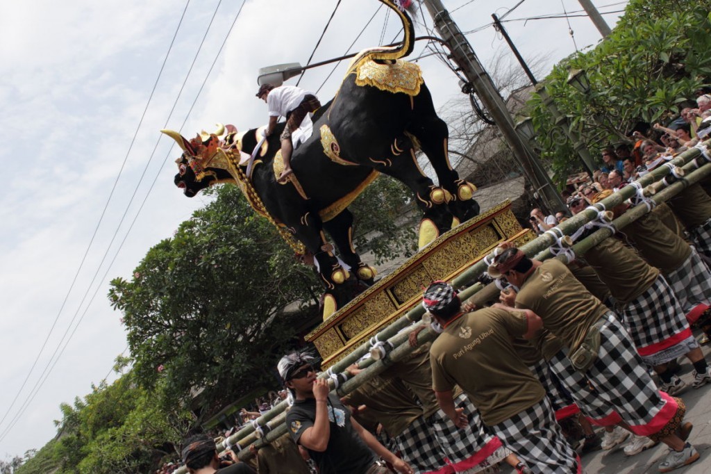 Bali cremation: men from the banjar carry a bull sarcophagus, with rider and MC.