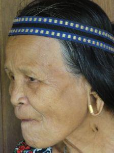 Old Lanahan lady chewing betel between toothless gums, with headband and an earring worn around the outside of the gaping hole in her earlobe. Balui River, Borneo, Sarawak, Malaysia.