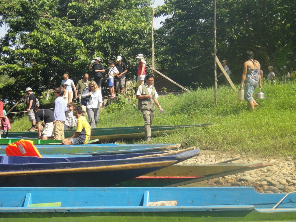 penan_woman_with_tourists_long_iman Young penan woman in sarong carrying water as tourists exit boats. Long Iman, Sarawak, Borneo.