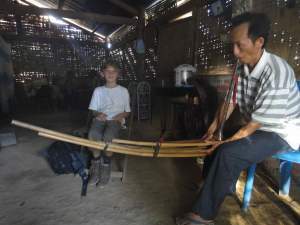 Hmong man in his house playing the qeej, while Z looks on.