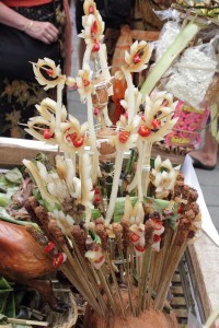 Bali cremation offerings including sticks of sate lilit and elaborate coloured rice dough figures in yellow and pink