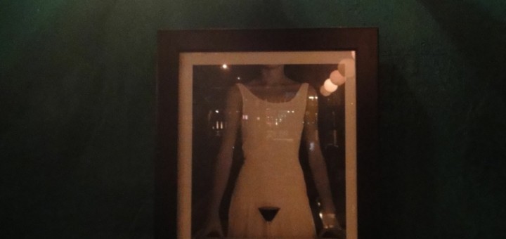 Framed picture on wall of girl in white glass holding martini glass at crotch level.