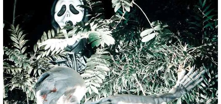 Child in scream mask over skeleton in bushes.