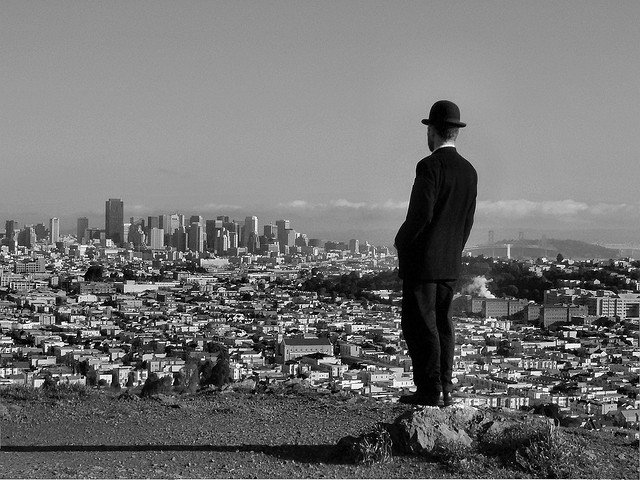Man in bowler hat looking out over cityscape.