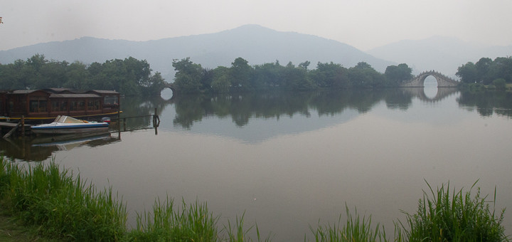 Boat, hills and bridge reflected in Xianghu Lake, Hangzhou.