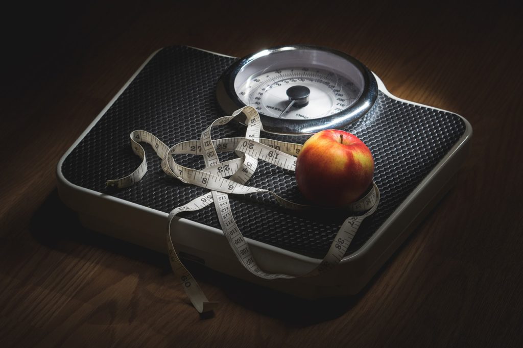 Apple and tape measure on a set of analogue scales.