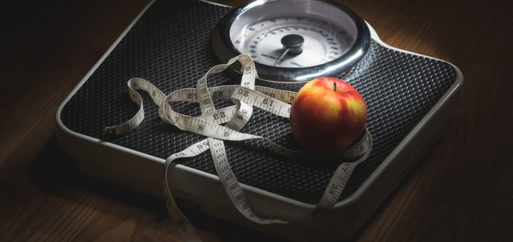 Apple and tape measure on a set of analogue scales.