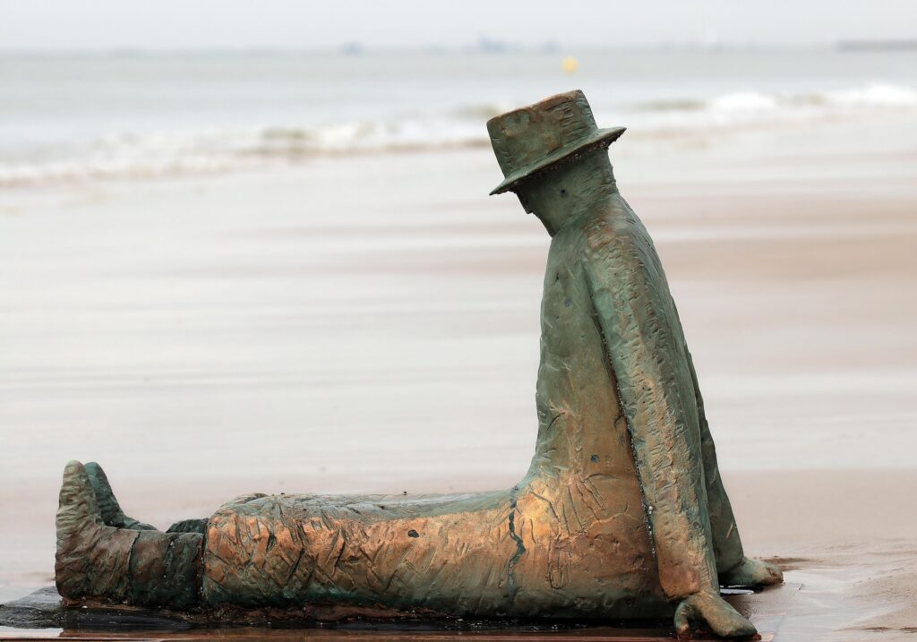 Confused-looking sculpture in a hat stranded on a beach.