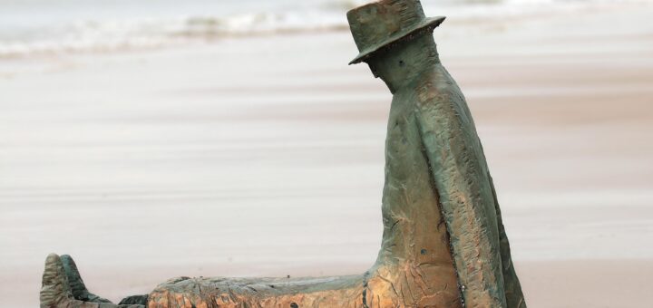 Confused-looking sculpture in a hat stranded on a beach.