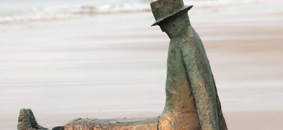 Confused-looking sculpture in a hat stranded on a beach.